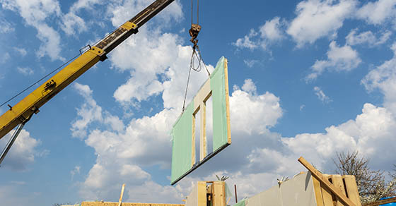 Process of construction new and modern modular house from composite sip panels. Crane with wall part against blue sky background
