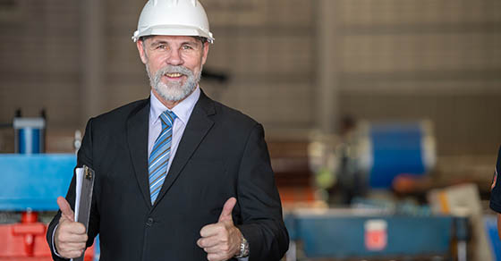 older owner engineer with beard mustache on face standing smile with his arms crossed at construction factory site. Boss manager in suit show good thumb at factory industry site.