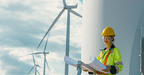 female engineer working outdoor with safety at wind turbines clean energy power station background, worker people with renewable energy technology for future concept.