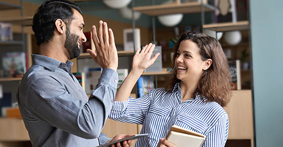 Two happy friendly diverse professionals, teacher and student giving high five standing in office celebrating success, good cooperation result, partnership teamwork and team motivation in office work.