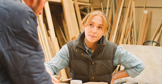 Close Up Of Male And Female Carpenter Working In Woodwork Workshop Discussing Plan Together